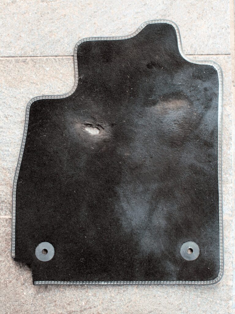 Why the Choice of Materials Matters: Impact on Durability, Cost, and Sustainability Damaged car mat with visible wear and tear